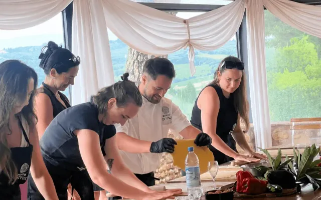 Chef e ospiti che preparano pasta fresca a un grande tavolo di legno