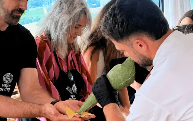 Un chef dépose à la poche une farce verte sur le carré de pâte d'un invité, lors d'un cours de cuisine au-dessus des collines toscanes