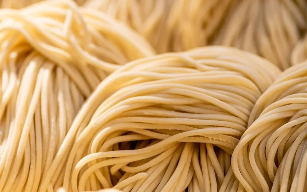 Thick, irregular strands of hand-rolled pici pasta on a wooden board