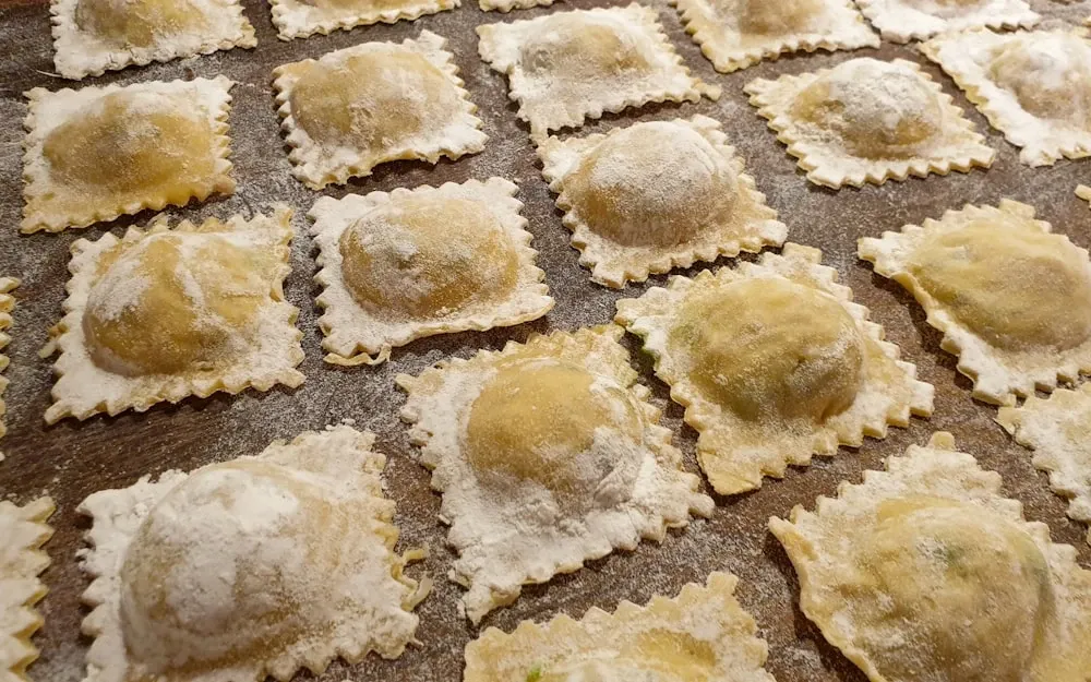 Rows of freshly made square ravioli with hand-pinched edges on a floured board