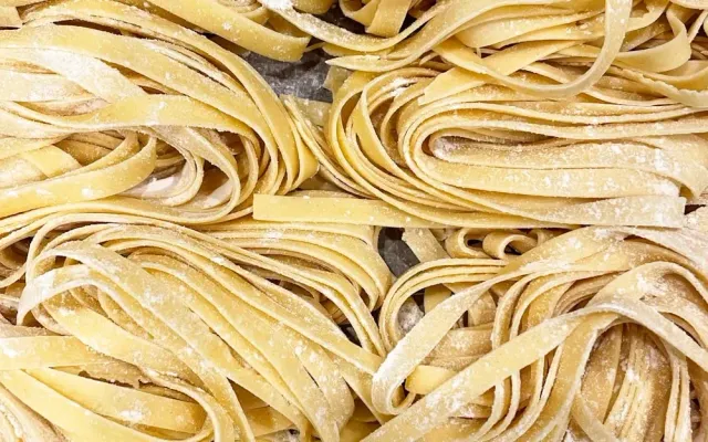 Nastri di tagliatelle fresche spolverate di farina su un tagliere di legno